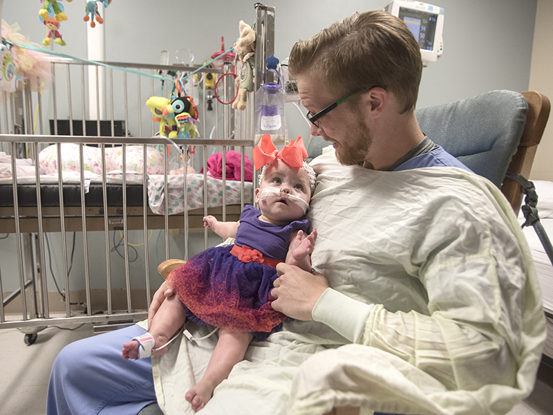 While Sonny Gunn, a second-year occupational therapy student, rocks Deavannah Bass, the infant's mother, Deanna, coaxes a smile from her toddler during the child's last day in the Neonatal Intensive Care Unit in the Winfred L. Wiser Hospital for Women and Infants.